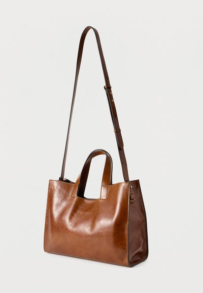 Καφέ λείο δερμάτινο τσάντα χειρός με κοντές λαβές και ρυθμιζόμενο μακρύ λουρί ώμου σε απλό φωτεινό φόντο.