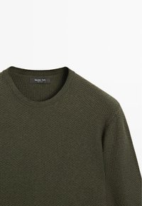 Maglione verde oliva lavorato a maglia con scollo rotondo. Presenta un motivo testurizzato e polsini a coste. Etichetta visibile all'interno del colletto.