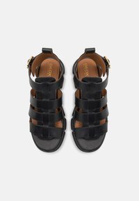Czarne skórzane sandały z wieloma szerokimi paskami na stopie, otwartym palcem i paskiem wokół kostki z zapięciem w kolorze złotym. Brązowa wkładka.