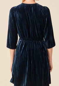 Vestido de terciopelo azul con un escote alto, mangas tres cuartos, tejido texturizado y cintura elástica. Falda suave y fluida.