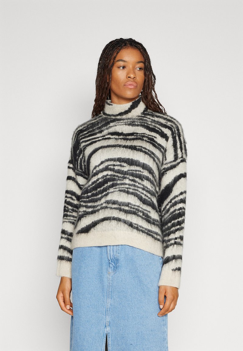 Gestreifter Rollkragenpullover in Schwarz und Weiß aus weichem Strickstoff, mit lockerer Passform und geripptem Saum, kombiniert mit einem hellblauen Denimrock.