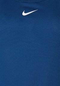 Niebieska koszulka sportowa wykonana z gładkiego materiału, z okrągłym dekoltem; na górze po lewej stronie umieszczone jest białe logo Nike.