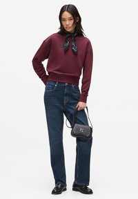 Bordeaux sweatshirt met ronde hals en zwarte sjaal, blauwe rechte spijkerbroek, zwarte tas met studs en zwarte schoenen met een lage hak.
