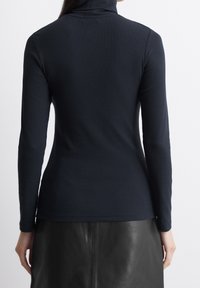 Maglia a collo alto navy realizzata in tessuto a coste, con maniche lunghe e silhouette aderente. Il bordo inferiore è leggermente curvato.