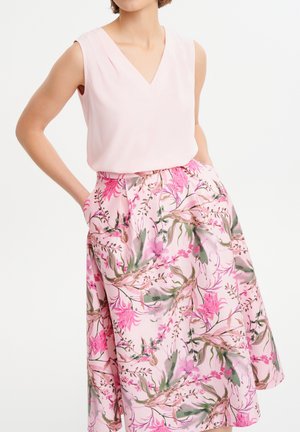 Blusa senza maniche a scollo a V di colore rosa chiaro abbinata a una gonna a fiori nelle tonalità di rosa, verde e beige, con tasche laterali.