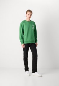 Grön sweatshirt i en mjuk bomullsmix; har rund halsringning, ribbade ärmslut och entryckt design på bröstet. Matchas med svarta jeans och vita sneakers.