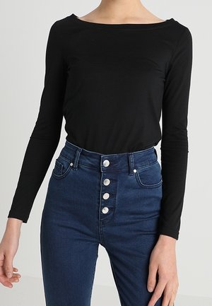 Black long-sleeve top with a wide neckline, paired with high-waisted dark blue jeans featuring five silver button closures and two front pockets.
