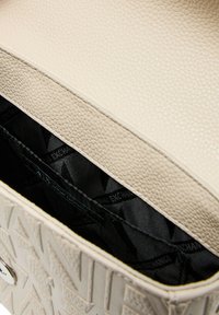 Borsa a tracolla in pelle beige con texture e motivo geometrico, aperta su un interno foderato in nero che presenta più scomparti e etichetta del marchio.