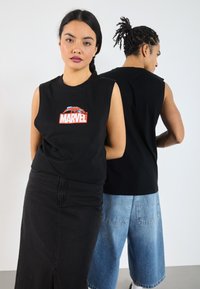 Must have musta särk, millel on punane ja sinine Marveli logo ees. Modell kannab musta seelikut; teine kannab taga teksapükse.