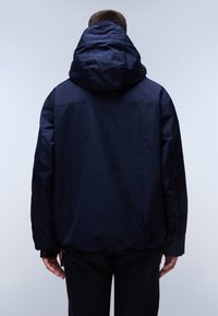 Námořnická modrá bunda s velkou kapucí, s hladkým matným povrchem, elastickými manžetami a mírně volnějším střihem.