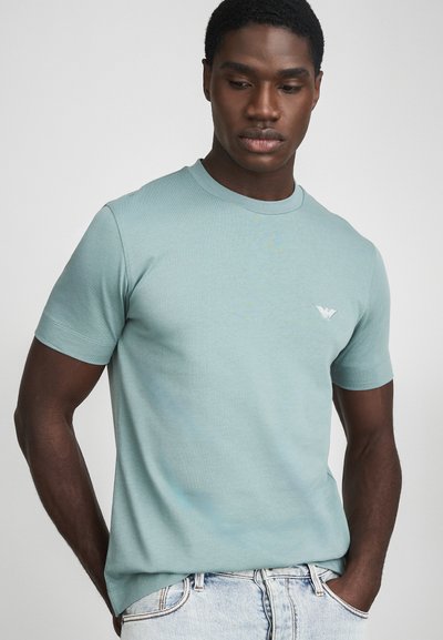 T-shirt bleu clair à manches courtes en coton doux, avec un col rond et un petit logo brodé sur la poitrine.