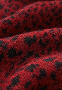 Sarkans un melns leoparda raksts audums ar mīkstu, pūkainu tekstūru; raksts ietver neregulāras melnas plankumiņus uz bagātīgas sarkanas fona.