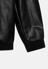 Manche en cuir noir avec une texture lisse, présentant un poignet noir côtelé à l'extrémité. Le design est simple et épuré.