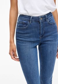 Jeans de mezclilla azul de tiro alto con un ajuste elegante, un ligero efecto desgastado, diseño de cinco bolsillos y botón metálico en la cinturilla.