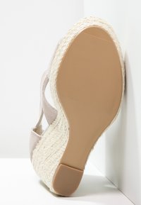 Sandalo con zeppa in espadrille, suola in juta intrecciata e suola in gomma, tomaia in suede beige, mostrato con la suola in alto su sfondo bianco.
