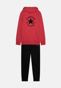Crvena dukserica s kapuljačom s crnim "Converse All Star" logom i dizajnom zvijezde; uparen s crnim trenirkama koje imaju mali logo na nozi.