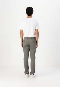 Graue Hose mit glatter Textur, fünf Taschen-Design und Gürtelschlaufen; kombiniert mit einem einfarbigen weißen Kurzarm-T-Shirt und weißen Sneakers.