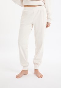 Roomkleurige, geribbelde joggingbroek met een elastische tailleband en taps toelopende enkels, gemaakt van zachte stof, ontworpen voor comfort en bewegingsvrijheid.