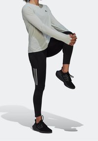 Ljusgrå långärmad träningsskjorta, svarta leggings med vita tre-randiga detaljer och svarta sneakers. Slät yta och figurnära design.