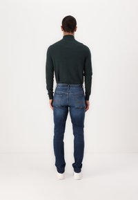 Cămașă lungă de culoare verde închis, asociată cu blugi din denim albastru. Blugii au un croi clasic, cusături vizibile și patru buzunare.
