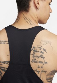 Schwarzes Sport-Tanktop mit Racerback-Design, aus glattem Stoff und verstärkten Nähten. Sichtbare Tattoos zieren den oberen Rücken des Trägers.