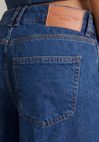 Niebieskie dżinsy z denimu z skórzaną metką "Marc O'Polo DENIM." Zwróć uwagę na miedziane szwy i wzór tylnej kieszeni.
