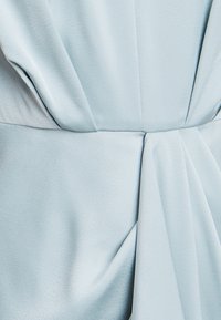 Svetlo modra satenastih obleka s nabranim detajlom na pasu. Gladka tekstura, prilegajoča prva in subtilen lesk.