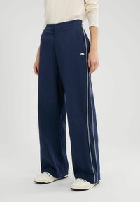 Marine wijde broek met witte zijstrepen, elastische tailleband en zakken, gemaakt van een gladde stof, gecombineerd met lichte schoenen.