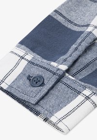 Ναυτικό και λευκό καρό πουκάμισο με μανσέτα που διαθέτει μπλε κουμπί, με υφασμάτινη υφή και αντίθετα μοτίβα στην ύφανση.