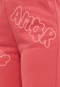 Ροζ ύφασμα με ανάγλυφα γράμματα σε σχήμα φυσαλίδων που σχηματίζουν τη λέξη "AIR" και μέρος ενός ανάγλυφου σχεδίου με σύννεφο και ουράνιο τόξο σε ρούχο.