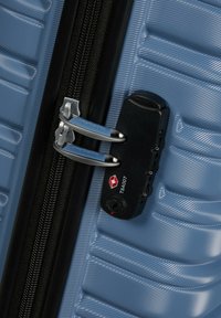 Valise rigide de couleur bleu clair avec texture rainurée, dotée d'un cadenas approuvé par la TSA et de tirettes de fermeture éclair en argent.