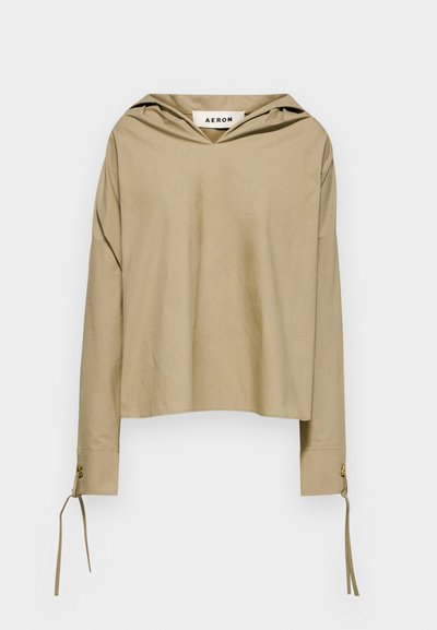 Haut beige à capuche avec manches longues, présentant un décolleté en V et des détails à nouer au niveau des poignets, fabriqué en tissu léger.