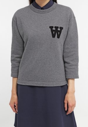 Sweatshirt gris avec des manches trois-quarts, arborant un "W" noir brodé sur la poitrine gauche. Tissu doux et coupe décontractée.