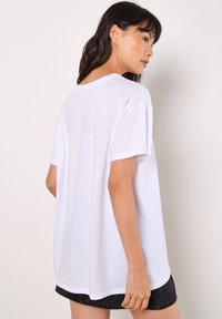 Weißes Baumwoll-T-Shirt mit lässiger Passform, kurzen Ärmeln und Rundhalsausschnitt, kombiniert mit einem schwarzen Jeansrock. Glatte Textur, schlichtes Design.