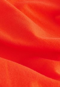 Lys orange stof med en glat, let tekstureret overflade. Materialet ser let ud og er foldet for at vise dybde og fald.