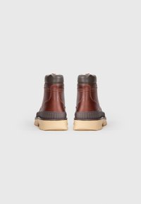 Bottes chelsea en cuir marron avec un col rembourré marron foncé et une semelle en caoutchouc clair, présentant un motif texturé sur les panneaux latéraux.