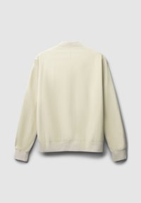 Giacca bomber beige chiaro con una texture liscia, colletto e polsini a coste, orlo leggermente elastico e dettagli di cucitura minimi.