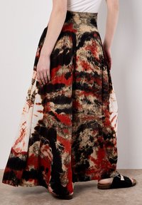 Jupe maxi avec un design plissé, présentant un motif abstrait audacieux en rouge, noir et beige. Fabriquée en tissu léger.