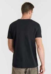 Camiseta negra de manga corta con cuello redondo, que presenta una textura suave y un ajuste casual, mostrada por la parte de atrás.