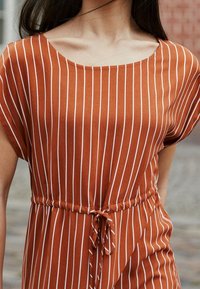 Rostfärgad klänning med vita vertikala ränder, rundad halsringning, korta ärmar, elastisk midja med knytdetalj och mjuk tygkvalitet.