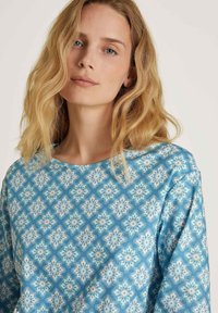 Blauw patroon top met een bloemenmotief in crèmekleurige en pastelkleuren, ronde halslijn en zachte stoftextuur.