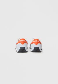 Reebok sporta apavi ar gaiši zilu zamšu augšdaļu, oranžiem akcentiem un melnu gumijas zoli ar teksturētu rakstu.