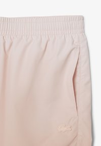 Pantaloni sportivi rosa chiaro con cintura elastica, tasche laterali e un piccolo logo ricamato in una tonalità contrastante. Texture liscia.