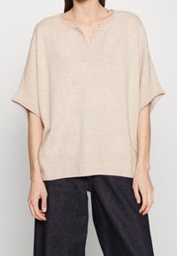 Beige gestricktes Oberteil mit V-Ausschnitt, kurzen Ärmeln und geripptem Saum. Weiche Textur mit lockerer Passform, ideal zum Schichten.