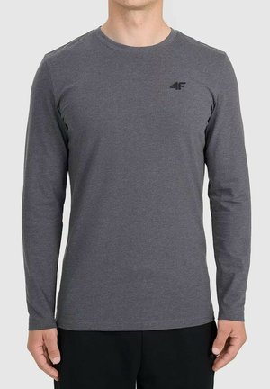 Mężczyzna w przylegającej ciemnoszarej koszulce z długim rękawem z małym czarnym logo "4F" na piersi, w połączeniu z czarnymi spodniami.