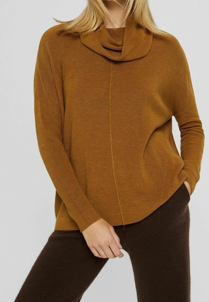 Pull jaune moutarde côtelé avec un col bénitier, coupe ample et poches latérales. Associé à un pantalon marron foncé en tissu texturé.