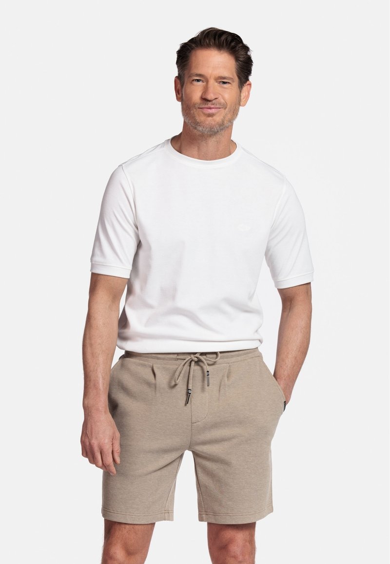 Witte T-shirt met korte mouwen, gecombineerd met beige joggingbroek met koordje. Het shirt heeft een ronde halslijn, terwijl de broek zijzakken heeft.