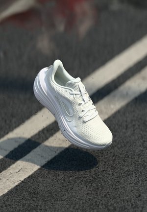 Hvit atletisk joggesko med teksturert mesh-overdel og polstret såle svever over asfalt med hvite veimerkinger.