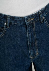 Jeans de mezclilla azul oscuro con cierre de botón, cinturilla con presillas y detalles de costura visibles. Incluyen bolsillos frontales y un ajuste estándar.