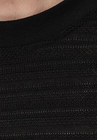 Czarna dzianina o fakturowanym wzorze z poziomymi paskami. Żebrowany czarny dekolt dodaje subtelnego detalu w designie.